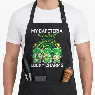 Patrick cafeteria aprons - Three gnomes in chef hats before a leopard and striped rainbow with shamrocks and stars — shown on a black cotton canvas apron against a white background
