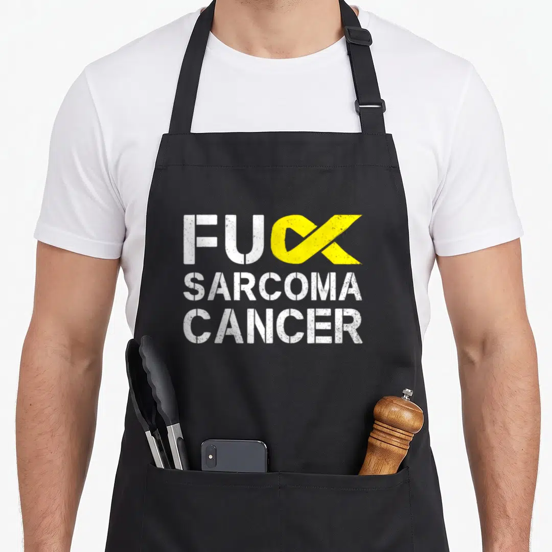 Sarcoma cancer ribbon apron - FUC SARCOMA CANCER text with yellow ribbon shaped like a K on black fabric — shown on a black cotton canvas apron against a white background