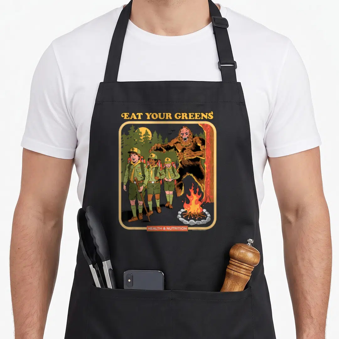 Steven dark green apron - Bigfoot looming behind three scouts with Eat Your Greens text — shown on a black cotton canvas apron against a white background
