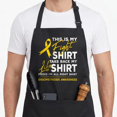 Endometriosis ribbon apron - Yellow awareness ribbon next to stacked white and yellow text reading THIS IS MY FIGHT — shown on a black cotton canvas apron against a white background