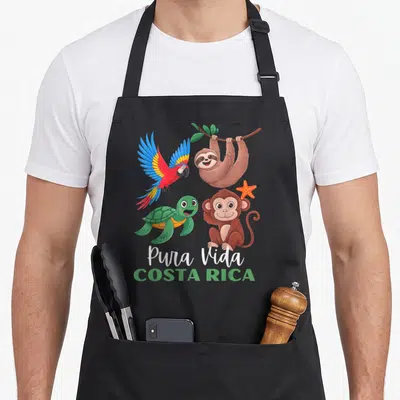 Parrot sloth apron - Four cartoon animals with Pura Vida Costa Rica text and orange starfish — shown on a black cotton canvas apron against a white background