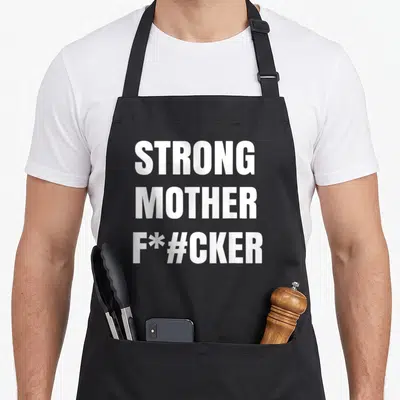 Strong strongman apron - White stacked text reading STRONG MOTHER F*#CKER in bold block letters — shown on a black cotton canvas apron against a white background