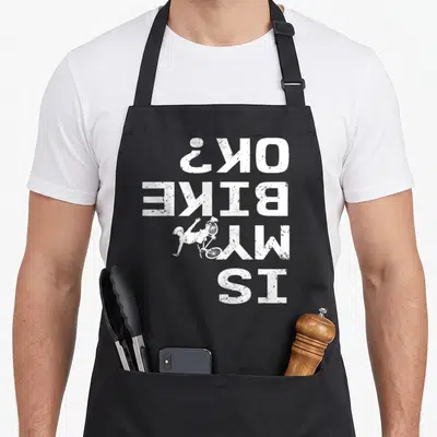 Sarcastic bike apron - Upside down white text Is My Bike Ok with fallen cyclist graphic — shown on a black cotton canvas apron against a white background