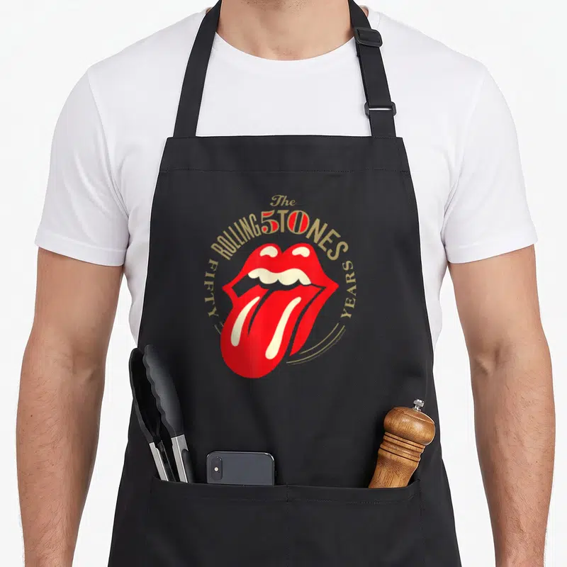 Tongue rolling stones apron for women - Red lips and gold Fifty Years text arranged in a circle around the center — shown on a black cotton canvas apron against a white background