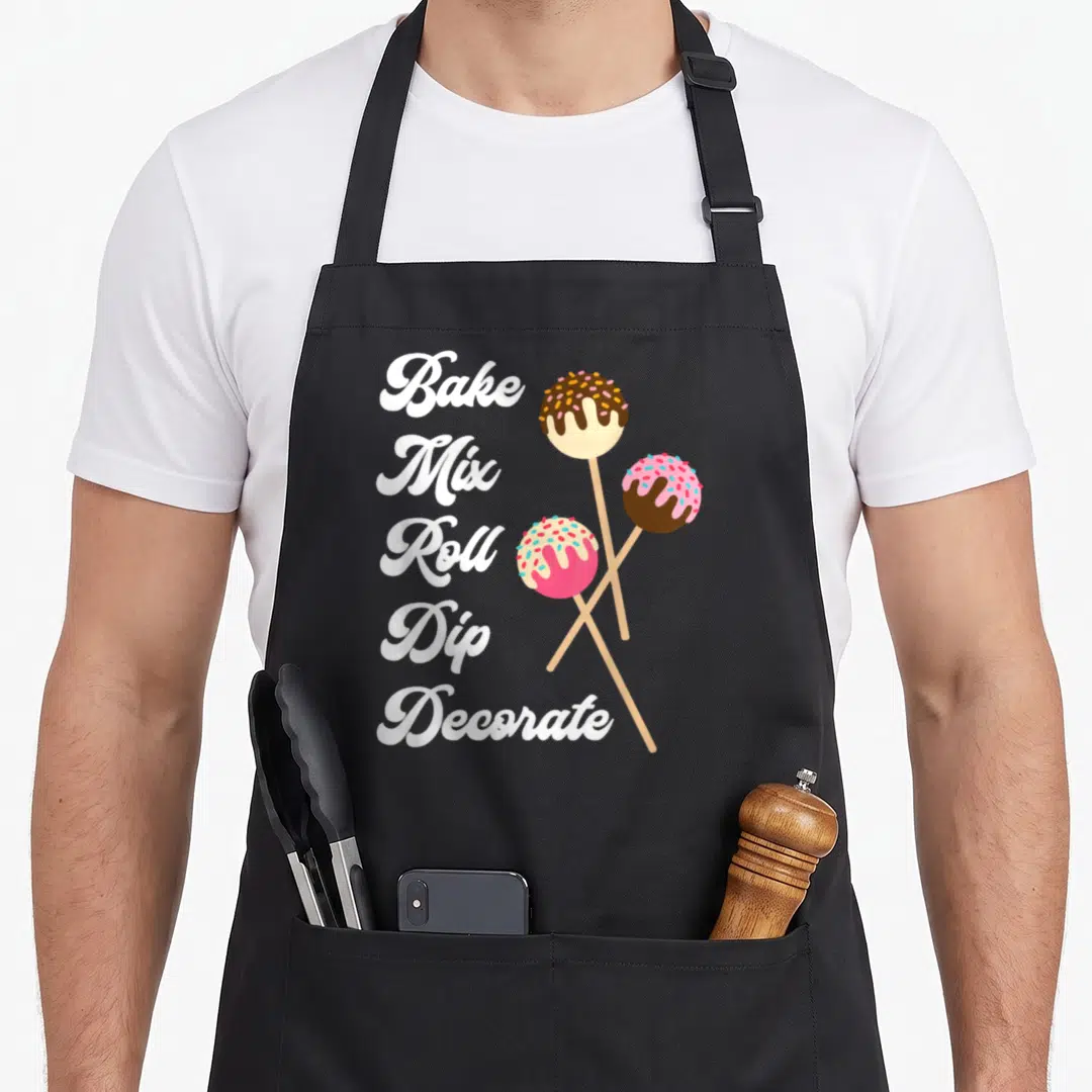 Mix bakers apron - Bake Mix Roll Dip Decorate text next to three cartoon cake pops on sticks — shown on a black cotton canvas apron against a white background