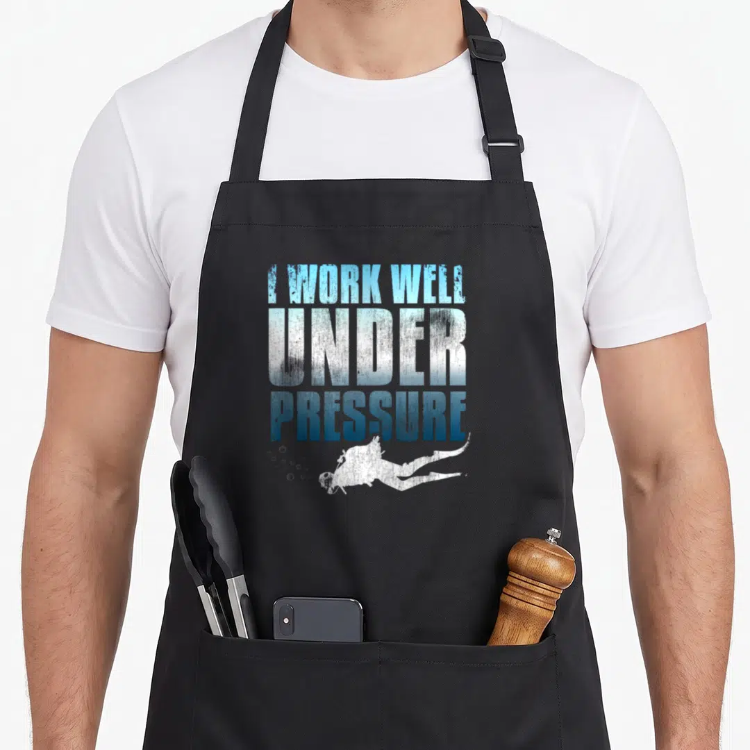 Well diving apron - I WORK WELL UNDER PRESSURE text with scuba diver silhouette and bubbles in blue gradient — shown on a black cotton canvas apron against a white background