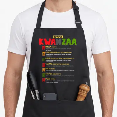 Outfit african american aprons - Joyous Kwanzaa text listing seven principles with red, yellow, green, and white symbols — shown on a black cotton canvas apron against a white background