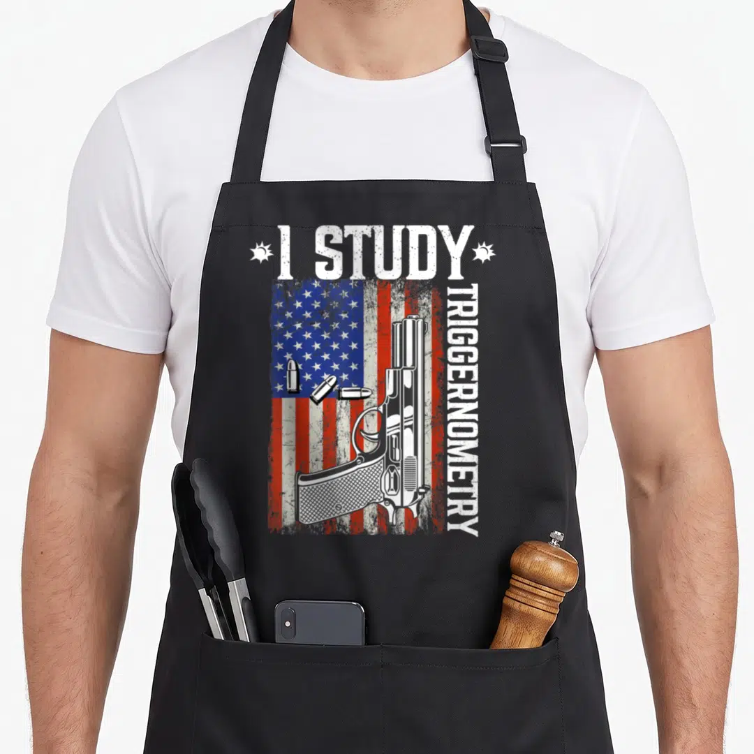 Study triggernometry gun apron - Distressed USA flag, centered handgun, three bullets, and vertical I Study — shown on a black cotton canvas apron against a white background