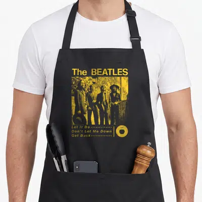 Retro garden apron - Yellow distressed Beatles photo with song titles and apple logo on black apron — shown on a black cotton canvas apron against a white background