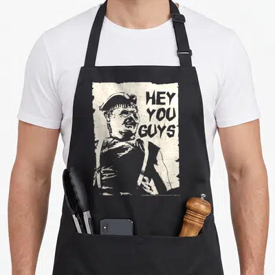 Hey sloth apron - Distressed beige rectangle with grey character portrait and stacked HEY YOU GUYS text — shown on a black cotton canvas apron against a white background