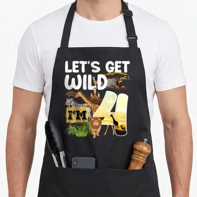 Animal 4th birthday apron - White LET'S GET WILD text above a sunset-filled number 4 with cartoon giraffes, zebras — shown on a black cotton canvas apron against a white background