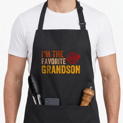Grandson grandchild apron - Stacked text I'm the favorite grandson with red official seal stamp — shown on a black cotton canvas apron against a white background