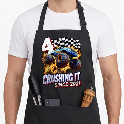 Monster 4th truck apron - Blue monster truck jumping through fire with number 4 and checkered flag — shown on a black cotton canvas apron against a white background