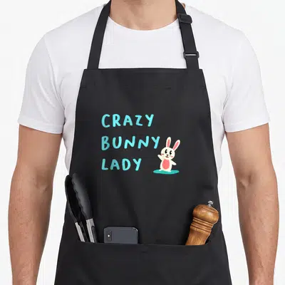 Cute animal bunny apron - Stacked cyan text reading CRAZY BUNNY LADY beside a white cartoon rabbit with pink ears — shown on a black cotton canvas apron against a white background