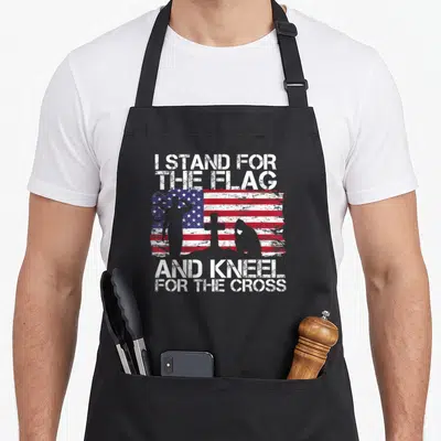 Flag cross apron - Distressed USA flag with saluting, cross, and kneeling silhouettes and white text — shown on a black cotton canvas apron against a white background