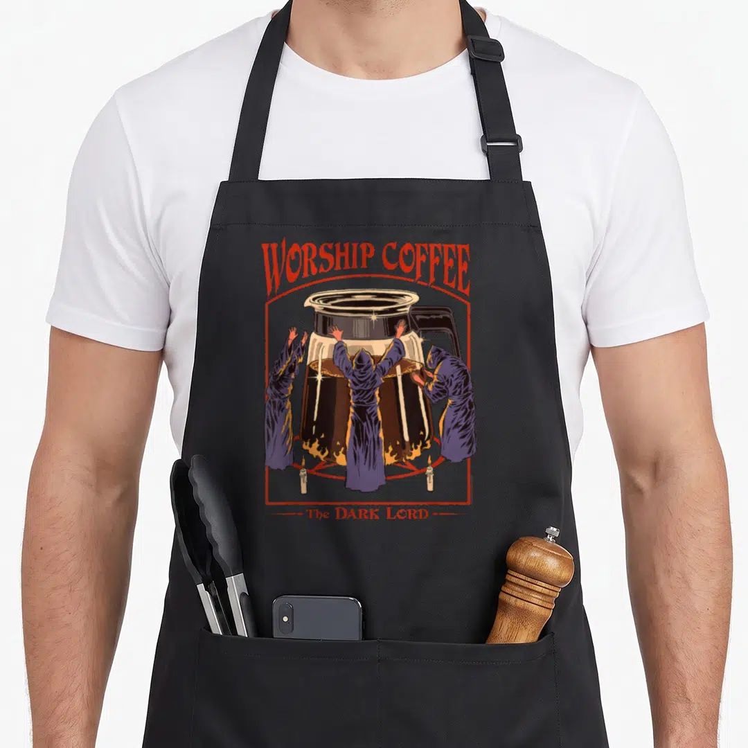 Steven coffee apron - Retro graphic of hooded figures worshipping a coffee pot with WORSHIP COFFEE text — shown on a black cotton canvas apron against a white background