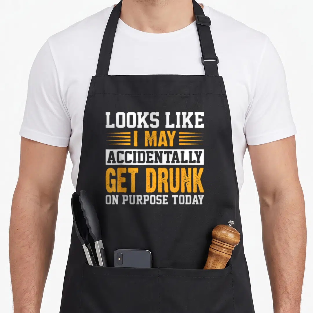 Drinking mens joke aprons - Stacked white and orange text reading Looks Like I May Accidentally Get Drunk On Purpose — shown on a black cotton canvas apron against a white background