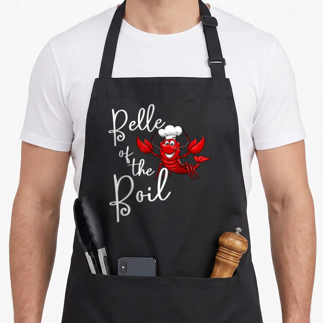 Belle lobster apron - Red cartoon lobster in chef hat next to white Belle of the Boil script text — shown on a black cotton canvas apron against a white background
