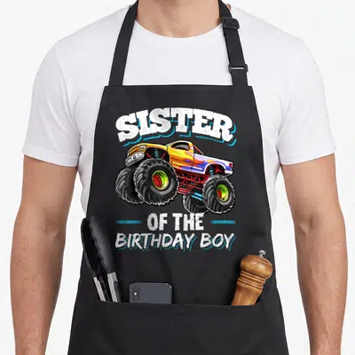 Sister truck apron - Sister of the Birthday Boy text with yellow and blue monster truck cartoon — shown on a black cotton canvas apron against a white background