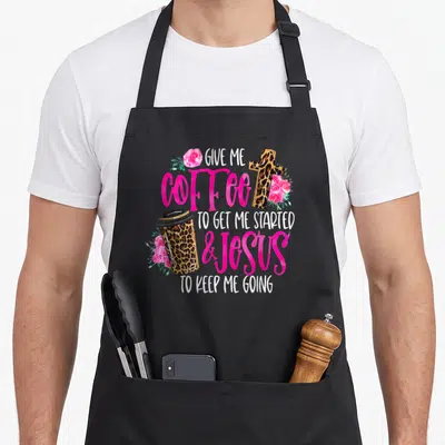Jesus coffee apron - Stacked text with leopard coffee cup cross and pink roses on canvas — shown on a black cotton canvas apron against a white background