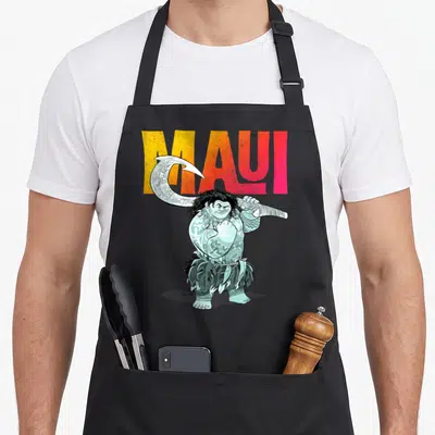 Pose novelty apron - Cartoon Maui holding fishhook in front of yellow to red MAUI text — shown on a black cotton canvas apron against a white background
