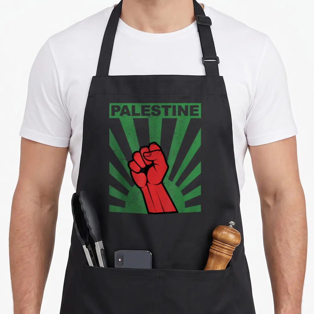 Propaganda palestine apron - Red raised fist on green sunburst rays with PALESTINE text in distressed style — shown on a black cotton canvas apron against a white background