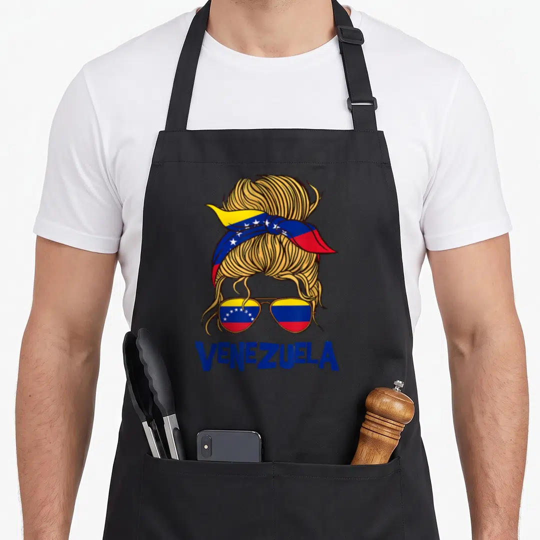 Latina messy aprons - Cartoon blonde messy bun with Venezuelan flag bandana, sunglasses, and VENEZUELA text in blue — shown on a black cotton canvas apron against a white background