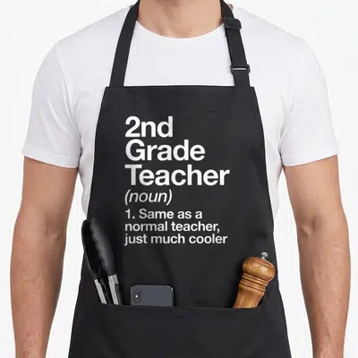 Definition 2nd apron - White stacked text defining 2nd Grade Teacher as normal but cooler — shown on a black cotton canvas apron against a white background