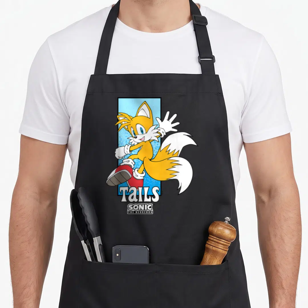 Tail spotlight apron - Tails character waving in front of blue rectangle with Sonic The Hedgehog logo text below — shown on a black cotton canvas apron against a white background