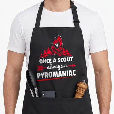 Scouting scout camping apron - Red and white campfire with logs, pine trees, and text ONCE A SCOUT always a PYROMANIAC — shown on a black cotton canvas apron against a white background