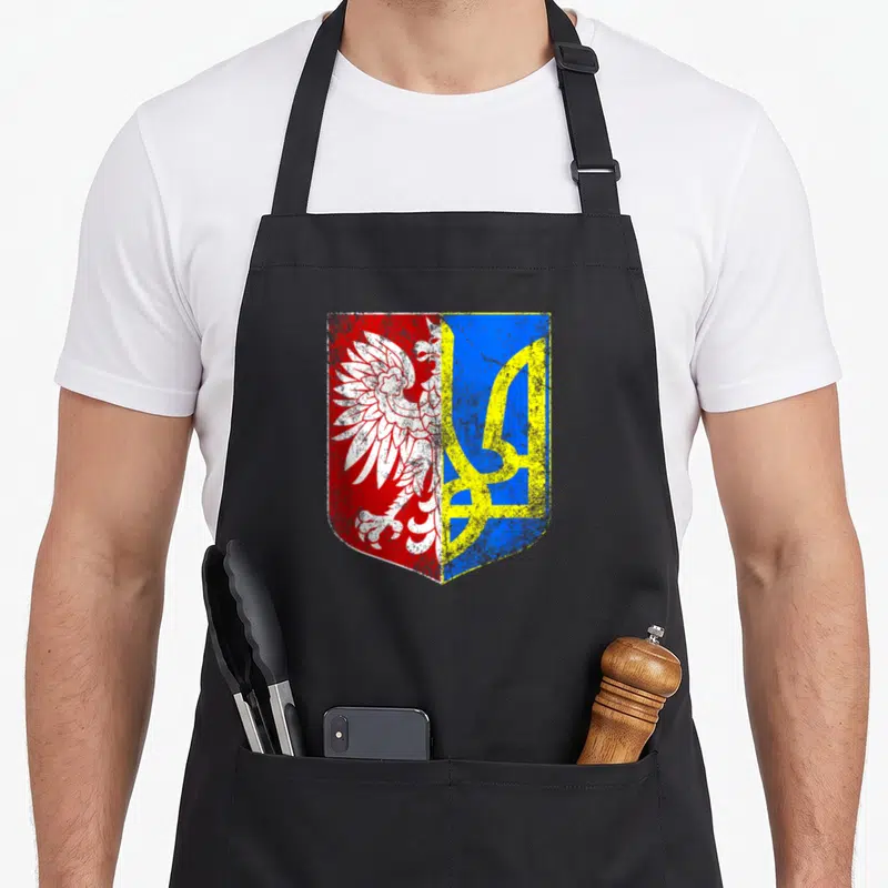 Ukrainian polish aprons - Distressed shield with white eagle on red and yellow trident on blue — shown on a black cotton canvas apron against a white background