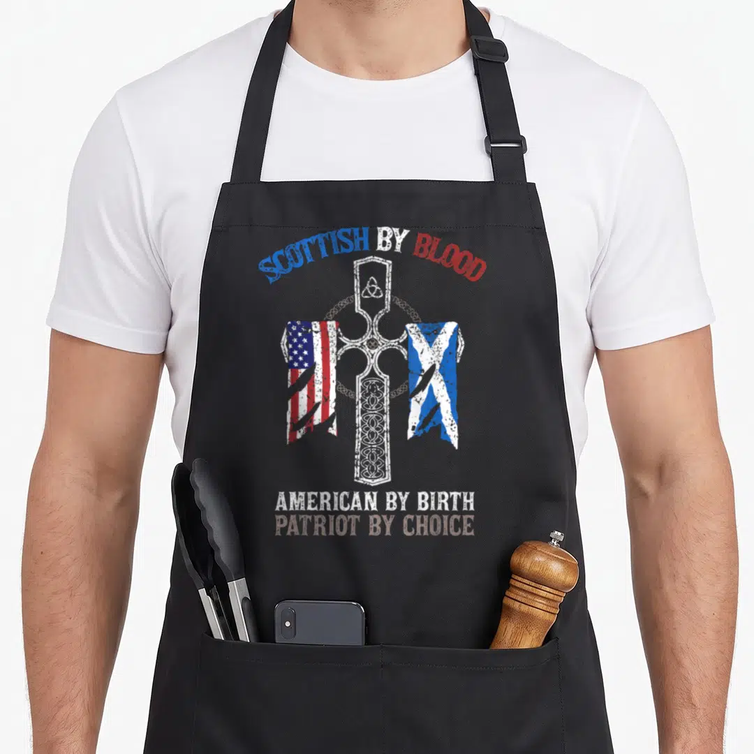 Patriot blood apron - Distressed Celtic cross with tattered US and Scotland flags and heritage text — shown on a black cotton canvas apron against a white background