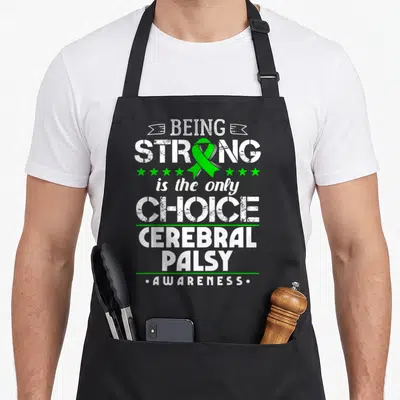 Cerebral ribbon apron - White and green typography reading Being Strong Is The Only Choice Cerebral Palsy Awareness — shown on a black cotton canvas apron against a white background