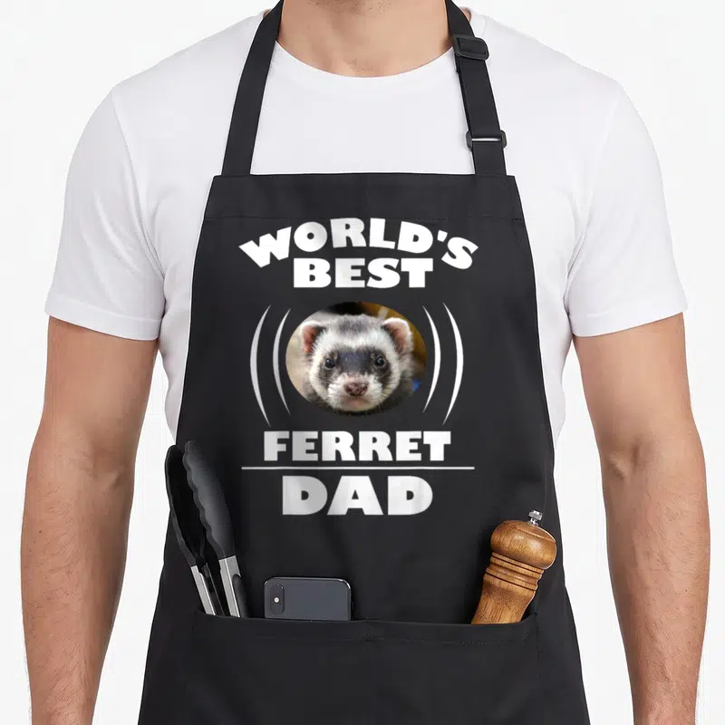 Ferret owner pet apron - WORLD'S BEST FERRET DAD text around a circular ferret photo with two white curved lines — shown on a black cotton canvas apron against a white background