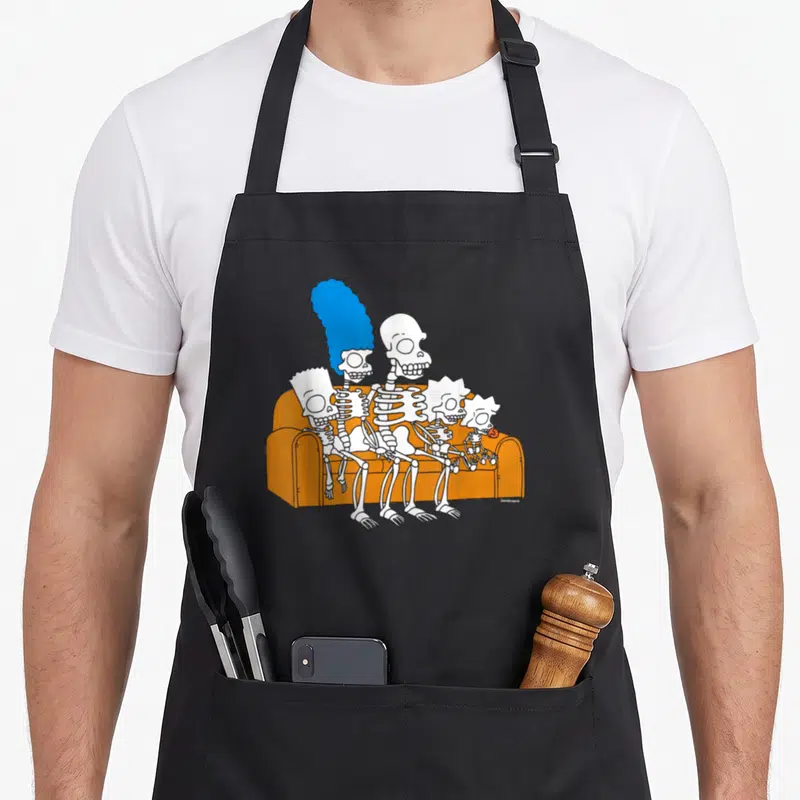 Treehouse skeleton apron - Five white skeletons sitting on orange sofa with blue hair cartoon art — shown on a black cotton canvas apron against a white background