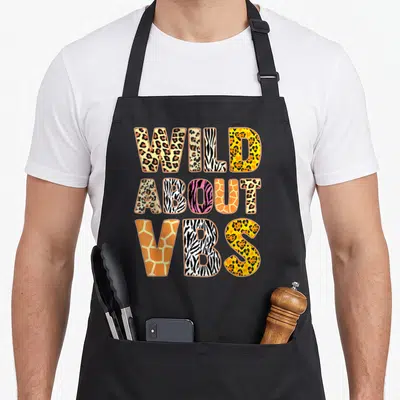 Wild vacation bible school apron - WILD ABOUT VBS text filled with leopard zebra and giraffe animal prints — shown on a black cotton canvas apron against a white background