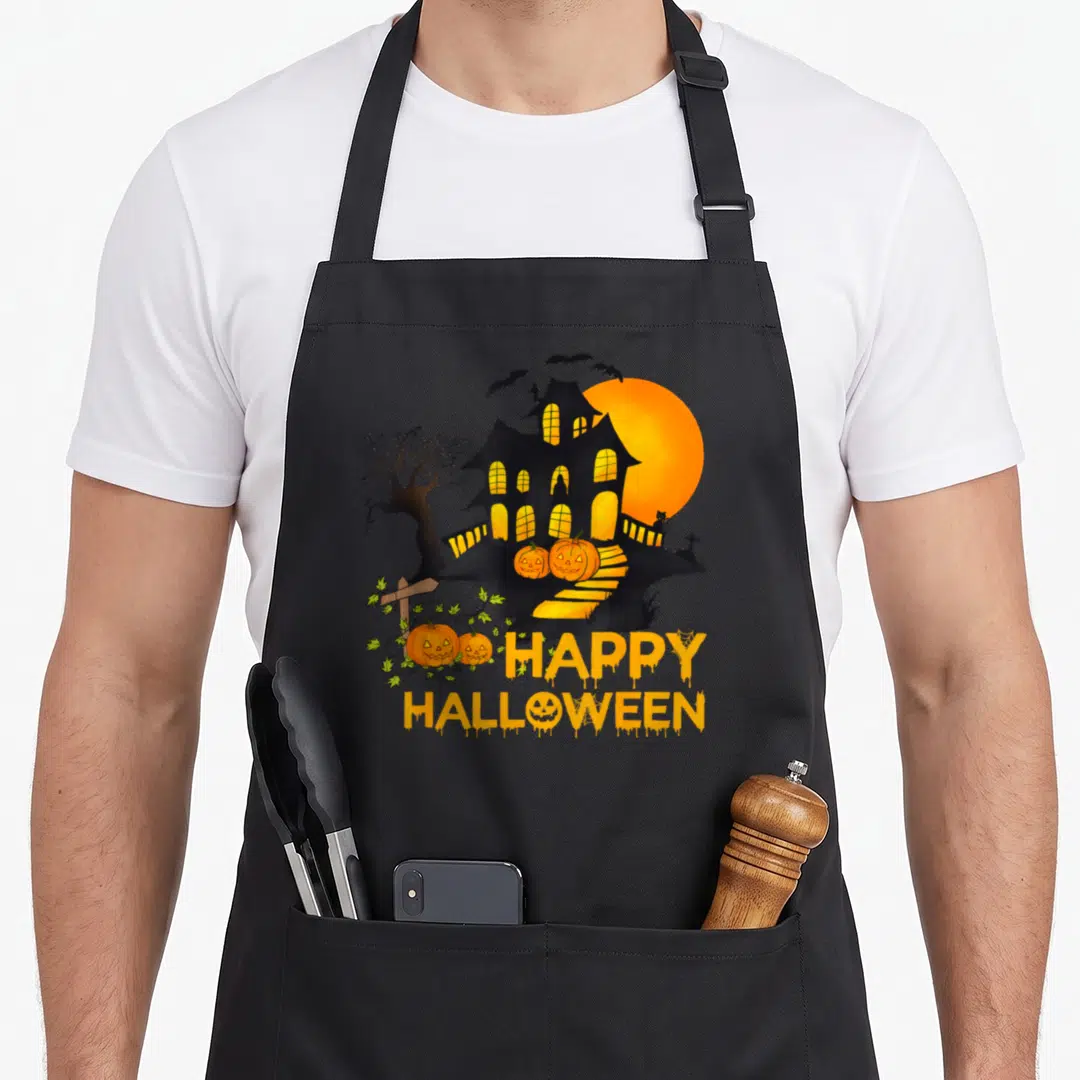 Pumpkin spooky apron - Haunted house with smiling pumpkins and dripping HAPPY HALLOWEEN text in orange and black — shown on a black cotton canvas apron against a white background
