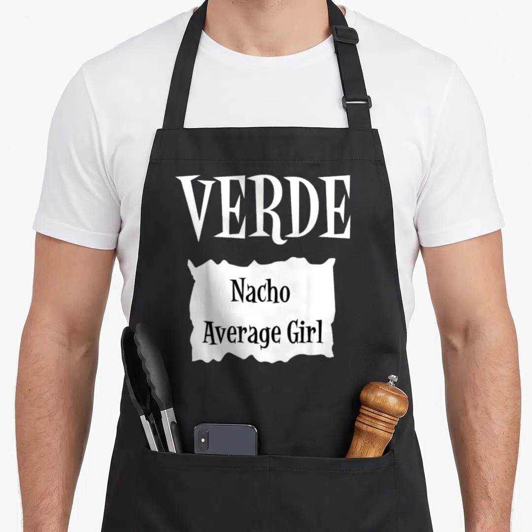 Verde taco apron - White torn paper graphic with VERDE Nacho Average Girl text in black typography — shown on a black cotton canvas apron against a white background