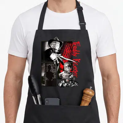 Nightmare elm apron - Freddy Krueger collage with red script text and metal claw glove in black grey and red — shown on a black cotton canvas apron against a white background
