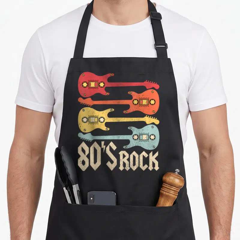 Guitar 80s apron - Four stacked electric guitars in red orange yellow and light blue with cassette details and 80'S — shown on a black cotton canvas apron against a white background