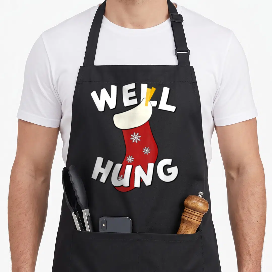 Hung womens christmas aprons - Red stocking with white snowflapes between WELL HUNG text — shown on a black cotton canvas apron against a white background