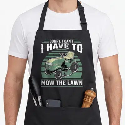 Sorry lawn apron - Green riding mower over green stripes with distressed white text SORRY I CAN'T I HAVE TO MOW THE LAWN — shown on a black cotton canvas apron against a white background