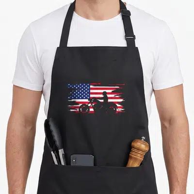 Flag motorcycle apron - Grey motorcyclist silhouette over distressed red white and blue American flag brush strokes — shown on a black cotton canvas apron against a white background