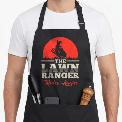 Ride rangers apron - Red sun silhouette of rider on mower with beige text THE LAWN RANGER Rides Again — shown on a black cotton canvas apron against a white background