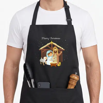 Scene merry christmas apron - Cartoon nativity scene with Merry Christmas text, stable, sheep, and star in brown blue — shown on a black cotton canvas apron against a white background
