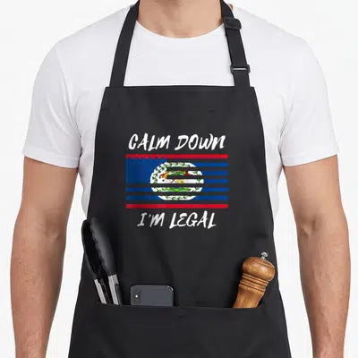 Illegal belizean apron - Calm Down I'm Legal text above and below a striped Belize flag design — shown on a black cotton canvas apron against a white background