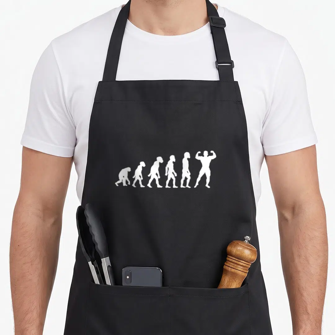 Human funny athletic apron - Six white silhouettes evolving from ape to muscular bodybuilder flexing — shown on a black cotton canvas apron against a white background