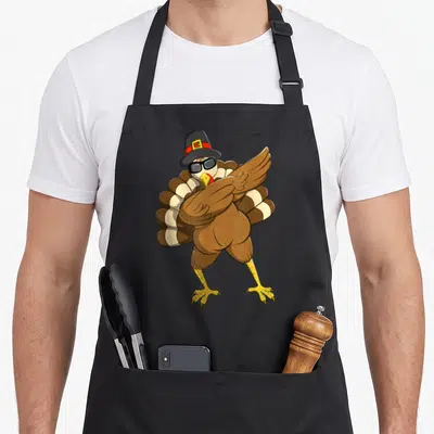 Funny dabbing thanksgiving day aprons - Cartoon turkey wearing sunglasses and a pilgrim hat with wings crossed — shown on a black cotton canvas apron against a white background