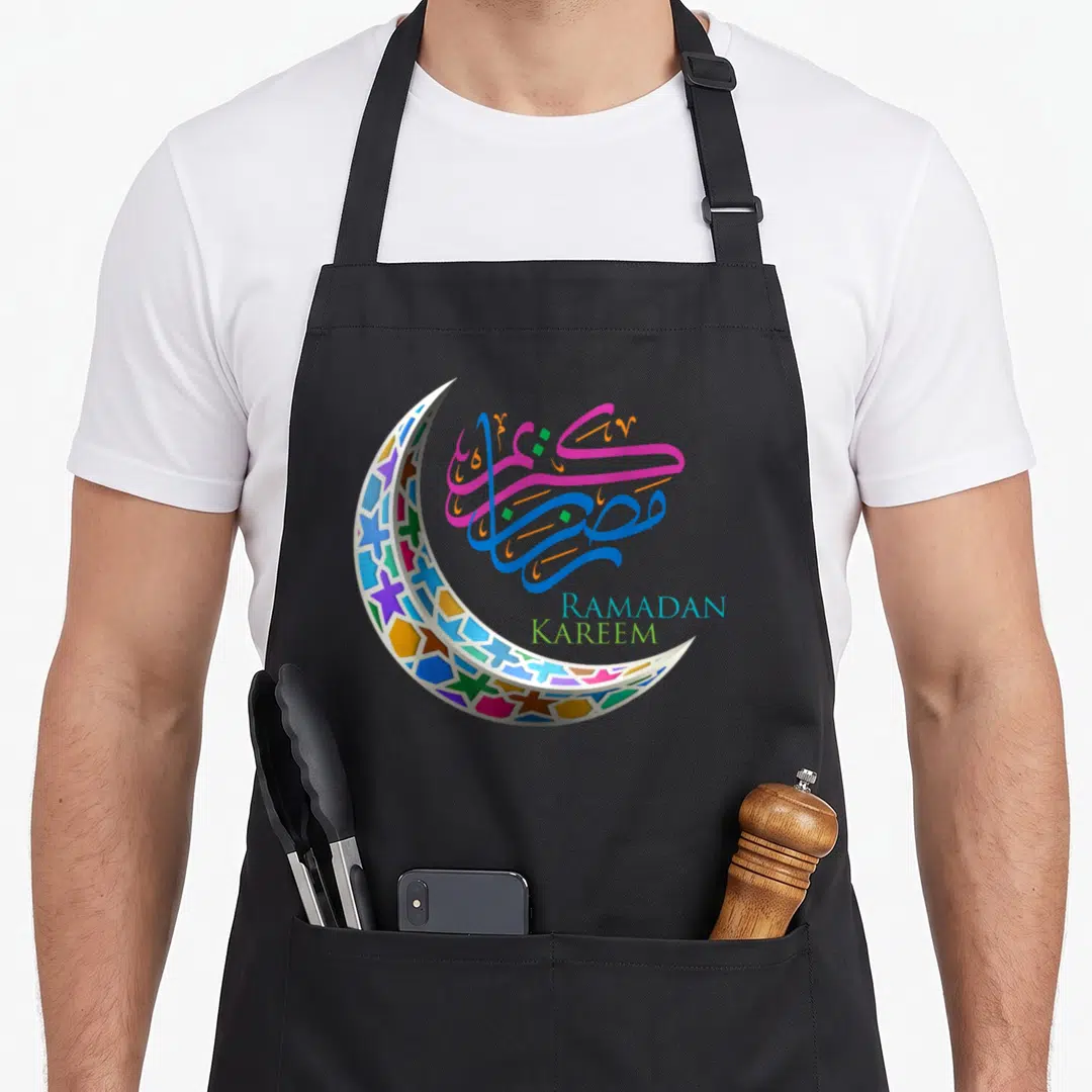 Ramadan holiday apron - Crescent moon with geometric stars and RAMADAN KAREEM text in blue pink green orange white — shown on a black cotton canvas apron against a white background