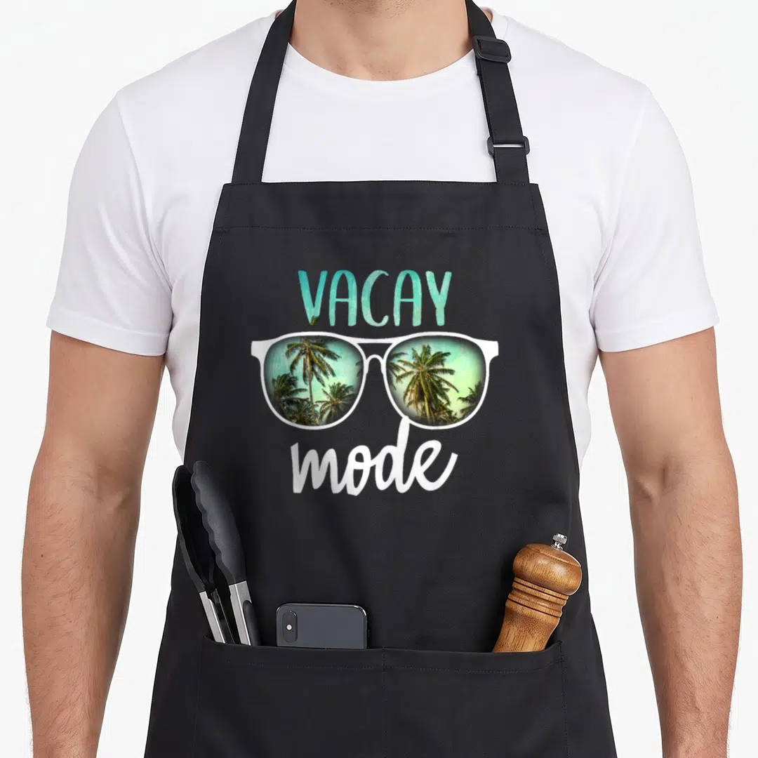 Vacay summer aprons - VACAY mode text above white sunglasses with palm tree reflection in teal lenses — shown on a black cotton canvas apron against a white background